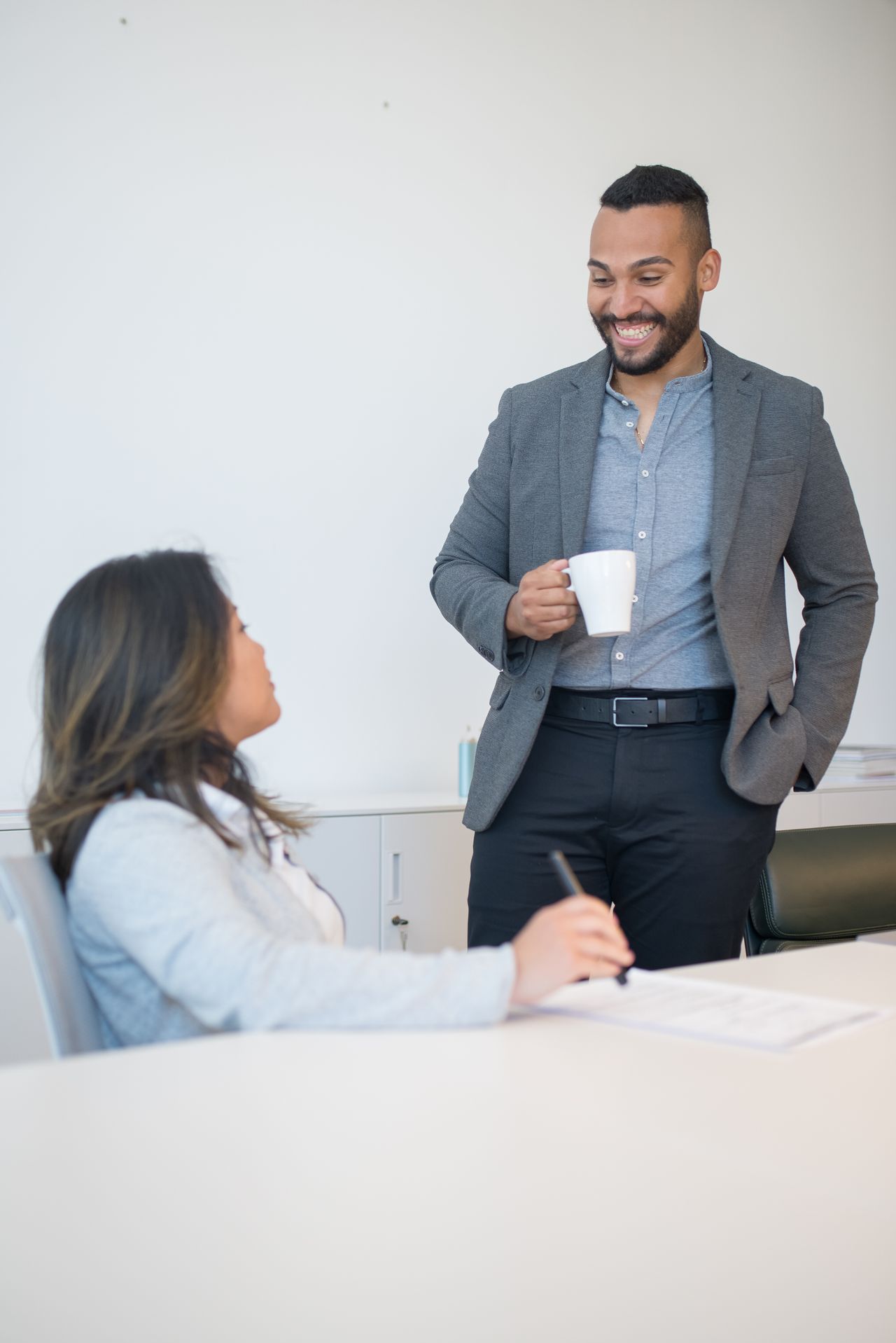 Two smiling colleagues having a relaxed conversation beside a desk.