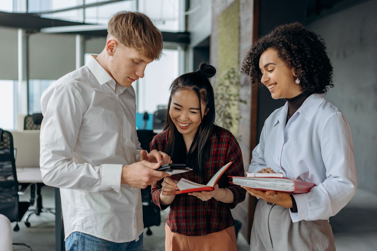 Three colleagues sharing notes and smiling together in a bright workspace.