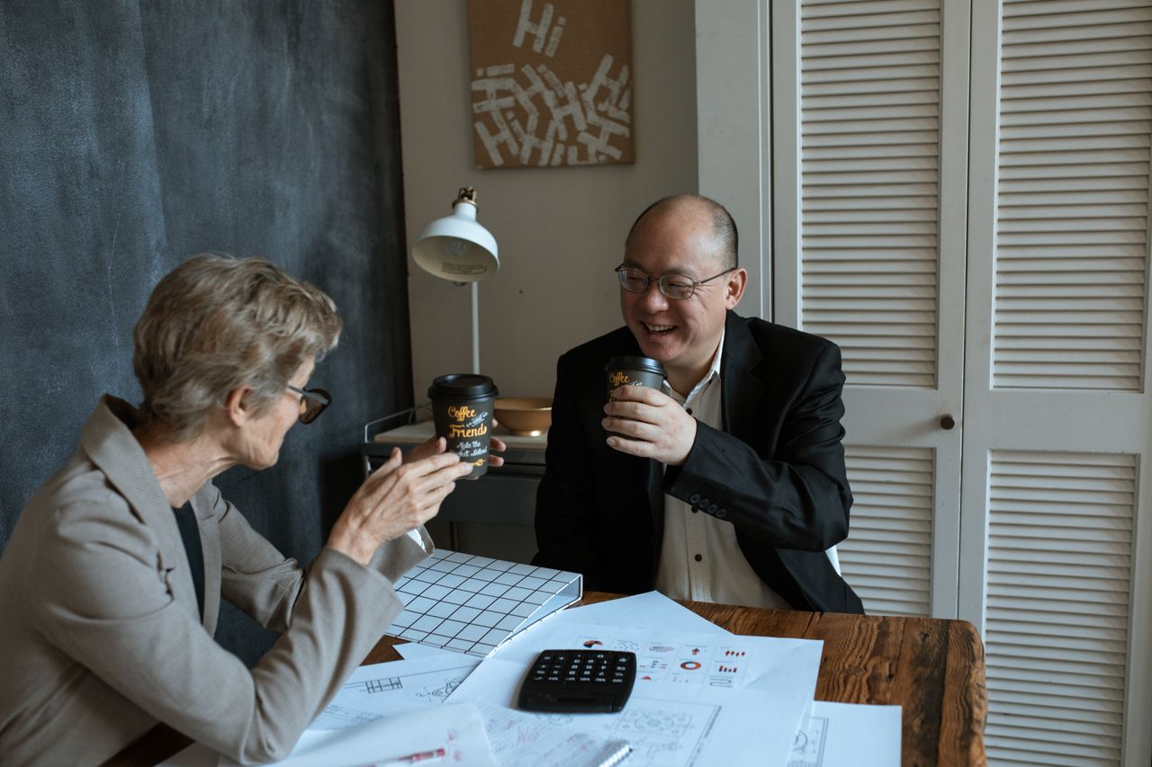 Two colleagues taking a coffee break beside their paperwork at a shared desk.